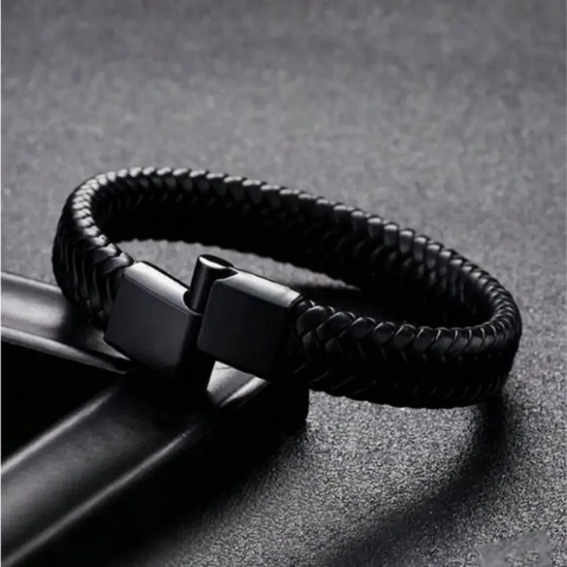 Black braided leather bracelet draped over an angular black leather stand, clasp shown open.