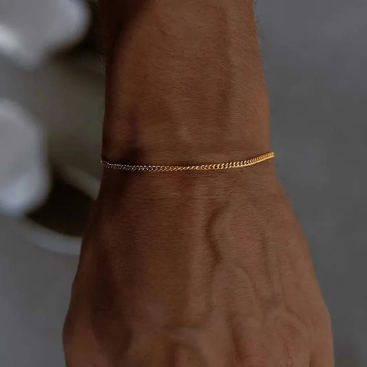 Wrist wearing the thin gold curb chain bracelet, natural daylight with a blurred grey background