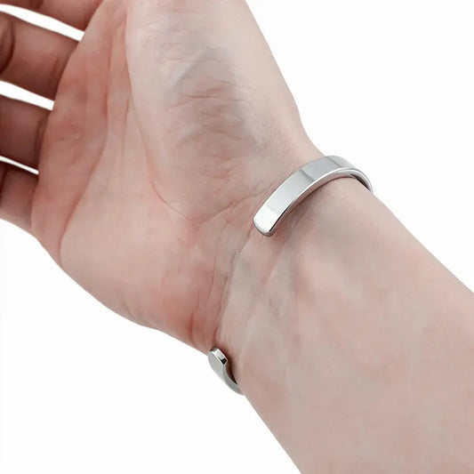 Silver stainless steel open cuff bangle worn on wrist, white background