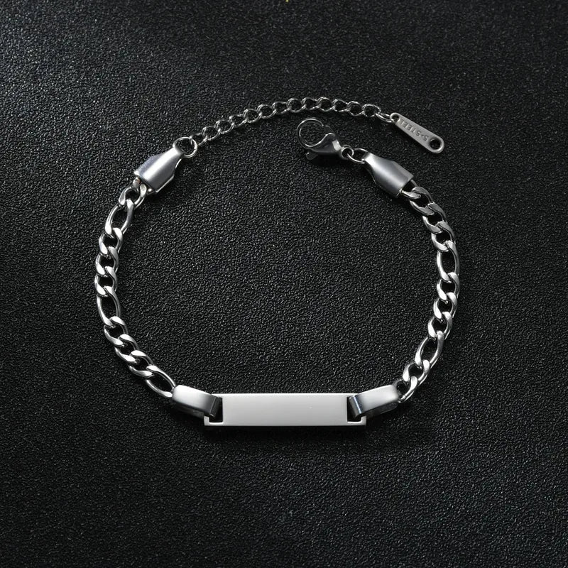 Silver curb-chain bracelet with a plain rectangular nameplate, smaller kids-sized scale, on a black textured background.