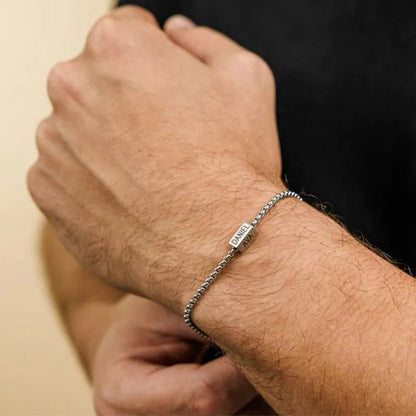 Man wearing the Customised Men's Bracelet – Kinship Box Chain Bracelet, engraved with two names on the tab.