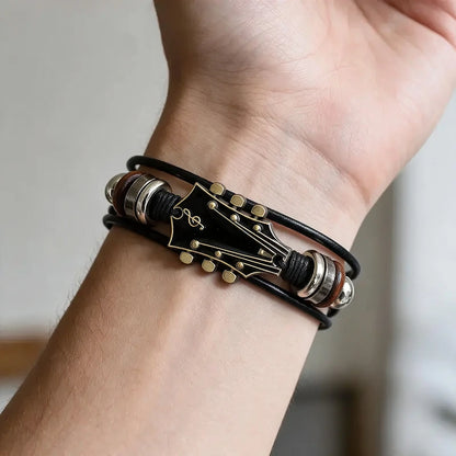 Black leather bracelet with a black enamel guitar-headstock charm and wood bead spacers, worn on a man's wrist.
