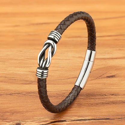 Brown braided leather bracelet with a polished stainless steel infinity-knot clasp, on a wood background