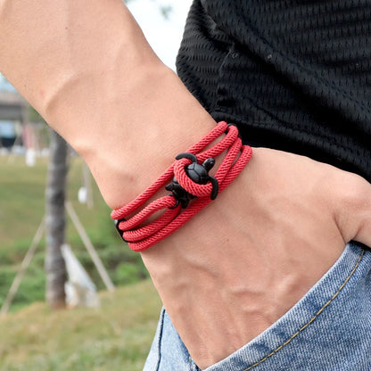 Sea turtle charm rope bracelet in red, worn on the wrist outdoors in a park