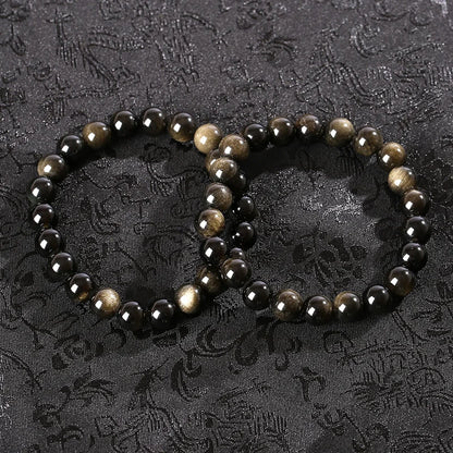 Two golden obsidian bead bracelets laid together on patterned fabric