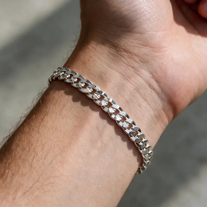 Silver diamond-cut flat curb chain bracelet worn on the wrist