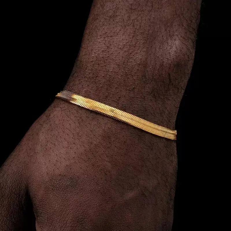 Wide gold flat herringbone chain bracelet worn on the wrist