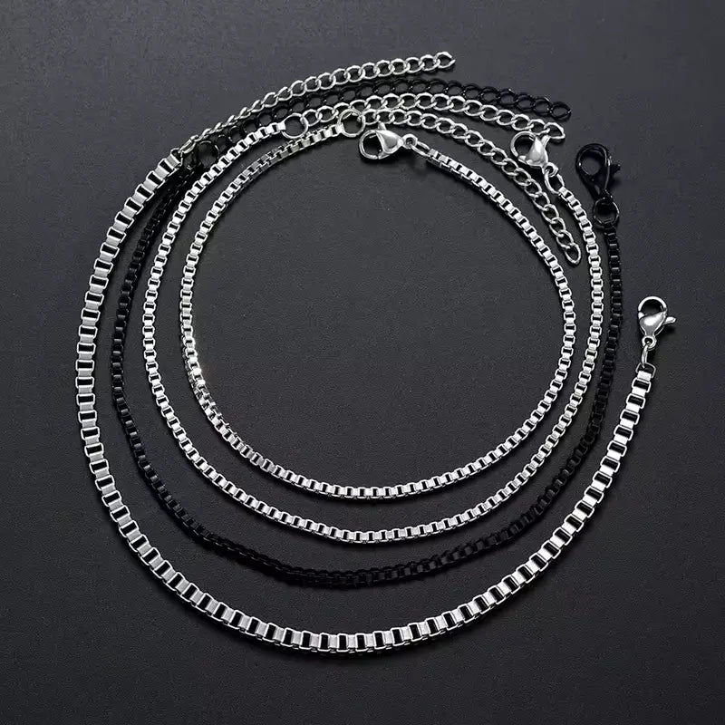 Four stainless steel box chain bracelets, three silver and one black, each with its own lobster clasp and extension chain, coiled together
