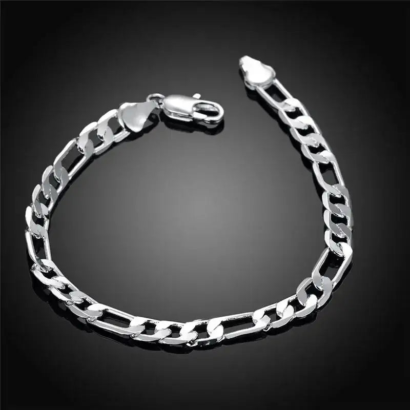 Silver figaro chain bracelet laid flat on a black background, showing the clasp