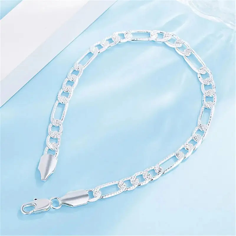 Silver figaro chain bracelet with textured curb links and lobster clasp, on a light blue background