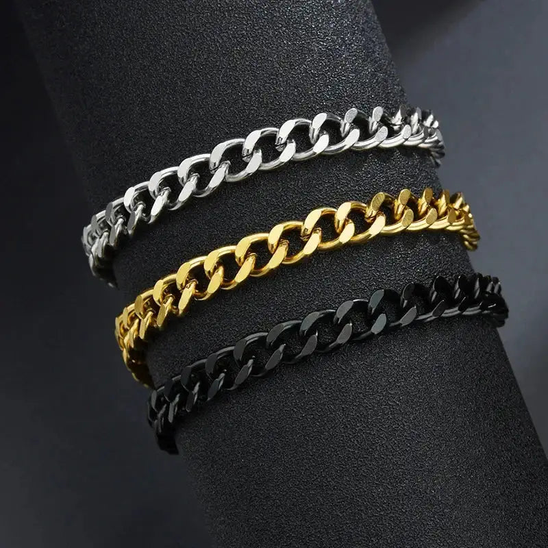 Silver, gold and black Cuban link chain bracelets stacked on a black leather display stand