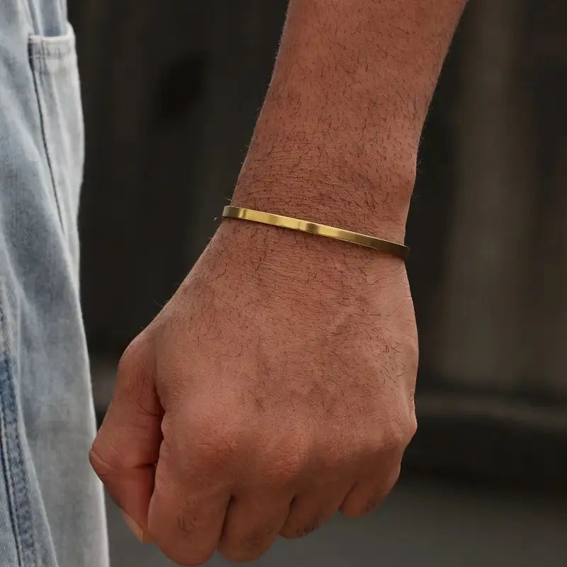 Gold open cuff bracelet worn on the wrist, hand in pocket