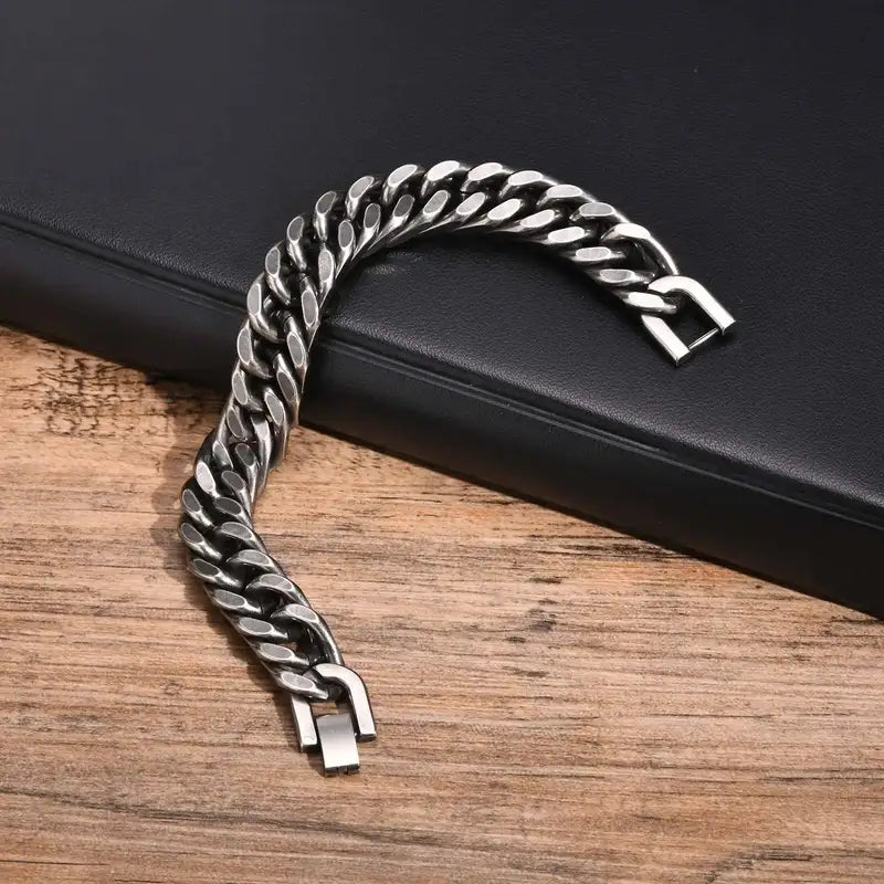 Close-up of the fold-over clasp mechanism on a gunmetal Cuban link bracelet, unclipped on a wood surface