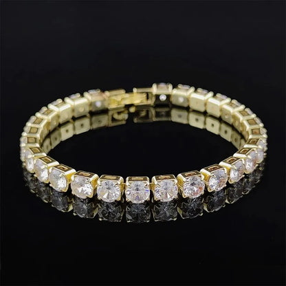 Gold tennis bracelet with square-set round cubic zirconia stones laid in a loop on a black background, clasp visible and stones reflected below.