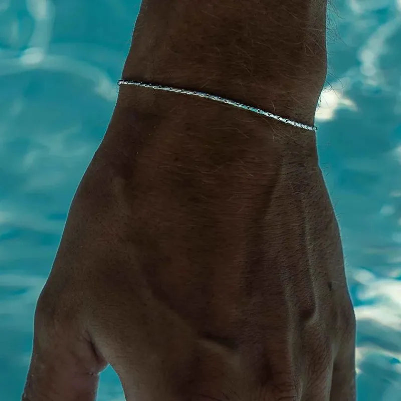 Silver-tone wire chain bracelet worn on the wrist poolside, with turquoise pool water in the background.