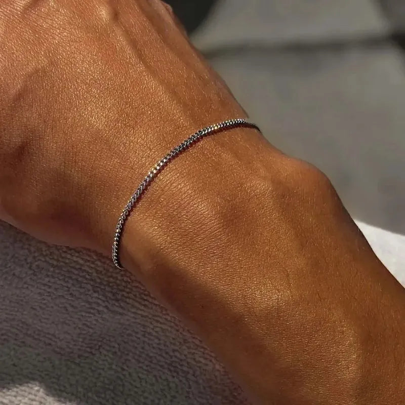 Close-up of a sunlit wrist wearing the thin silver curb chain bracelet, resting on a grey towel
