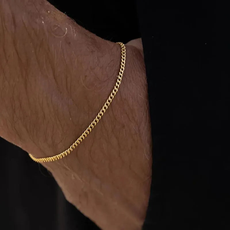 Wrist wearing the thin gold curb chain bracelet against a dark black background