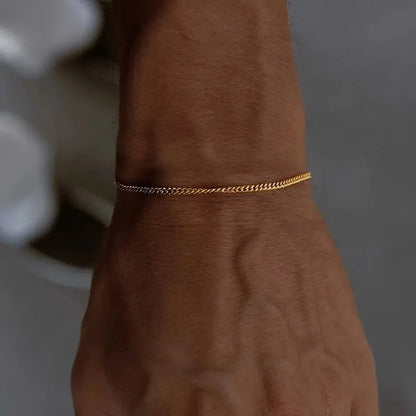 Wrist wearing the thin gold curb chain bracelet, natural daylight with a blurred grey background