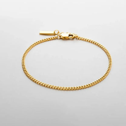 Thin gold Cuban curb chain bracelet with a small rectangular bar tag charm, on a plain white background