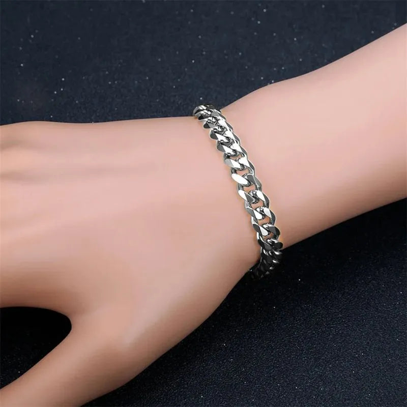 Silver-tone curb-link chain bracelet worn on a hand against a dark, glittery background.