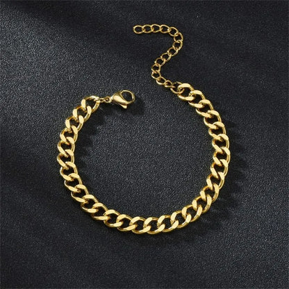 Gold Cuban chain bracelet laid flat in an oval shape on a black textured surface, with the lobster clasp and extension chain visible.