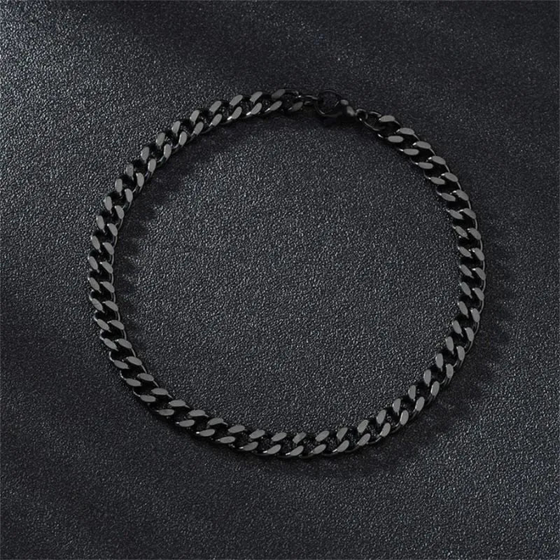Black-finish Cuban chain bracelet laid flat in a circle on a black textured surface, with the lobster clasp and extension chain visible.