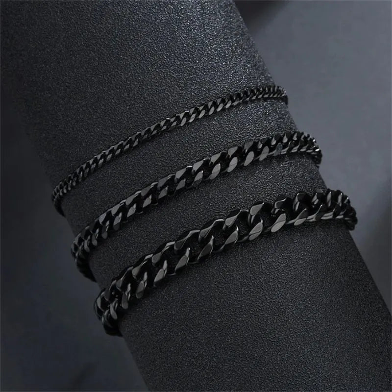 Three black-finish Cuban chain bracelets of increasing width draped around a black display cylinder, showing the range of available widths.