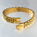 Gold jubilee-style watch link bracelet laid open on a light grey textured surface, showing the fold-over clasp unfastened