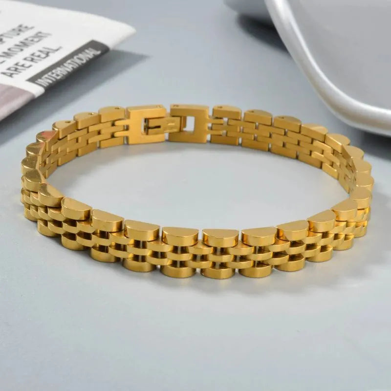 Gold watch link bracelet on a grey desk surface beside a folded newspaper and a white cup
