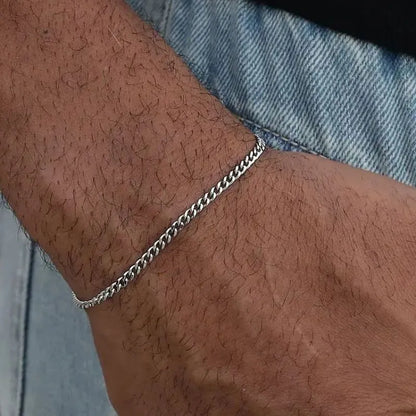 Silver-tone Cuban link bracelet worn on the wrist against a denim jacket sleeve.
