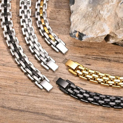 Four watchband-link bracelets in black, two-tone silver, gold, and two-tone gold finishes, laid diagonally on a wooden surface with a large stone prop.