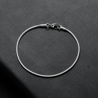Silver snake chain bracelet laid in a circle on a black leather surface, showing the lobster clasp.
