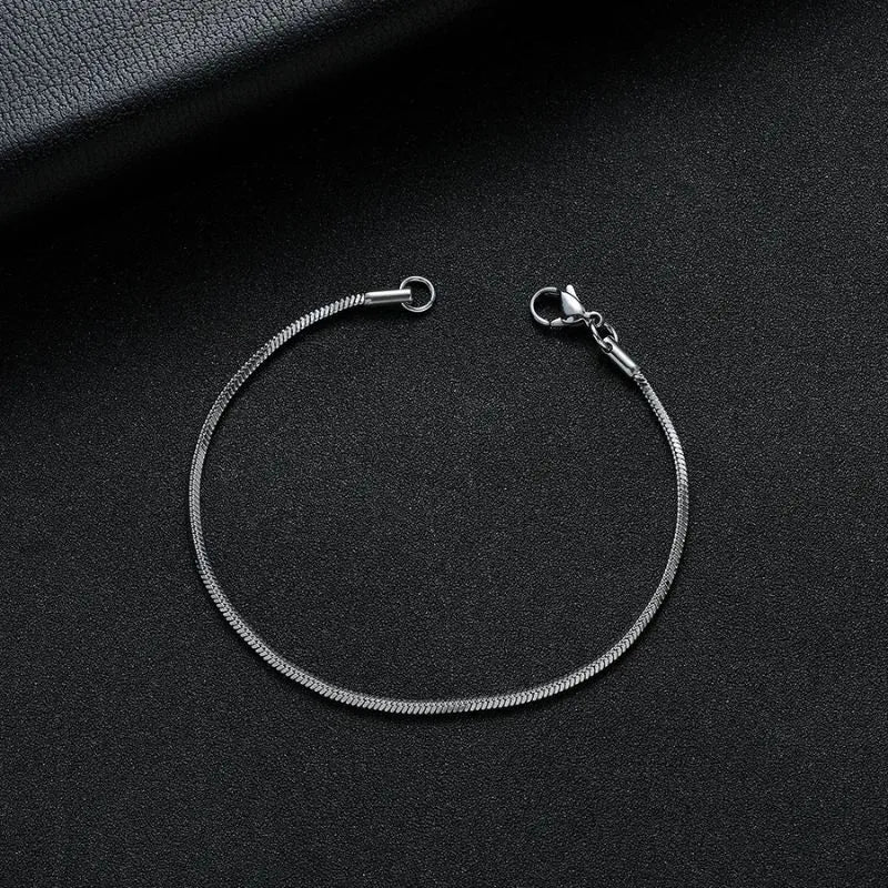 Silver snake chain bracelet shown open, laid in an oval on a black leather surface with a dark leather book prop.