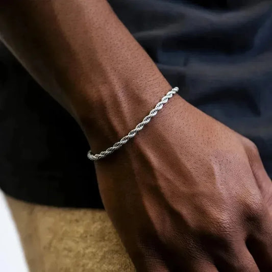 Silver twisted rope chain bracelet worn on the wrist, dark navy shirt in the background with tan shorts visible.