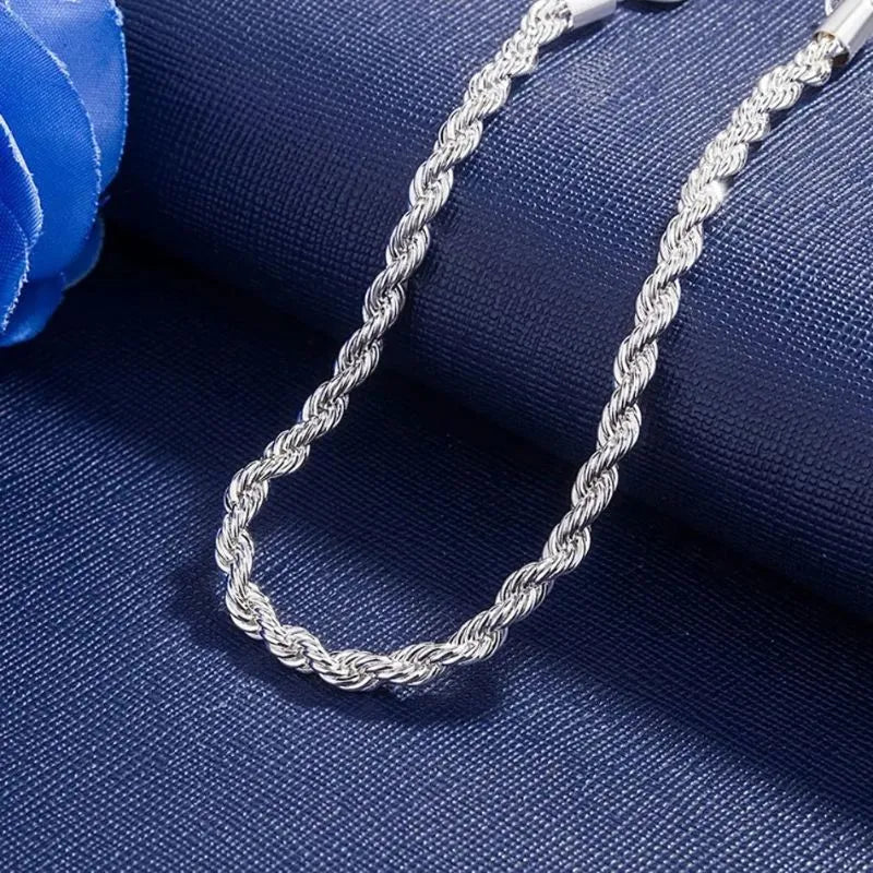 Silver twisted rope chain bracelet draped in a loop on a navy fabric backdrop, with a blue rose prop in the corner.