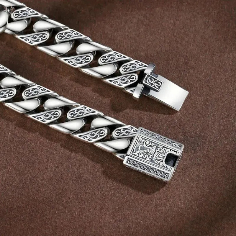 Close-up of the engraved Cuban-link chain and clasp, against a dark brown textured background.
