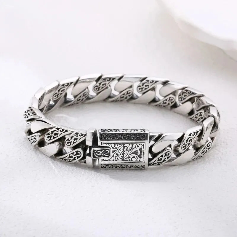 Engraved silver Cuban-link bracelet laid in an oval on a plain white background.