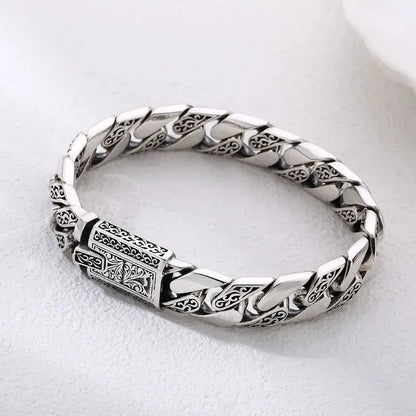 Engraved silver Cuban-link bracelet laid in an oval on a plain white background.