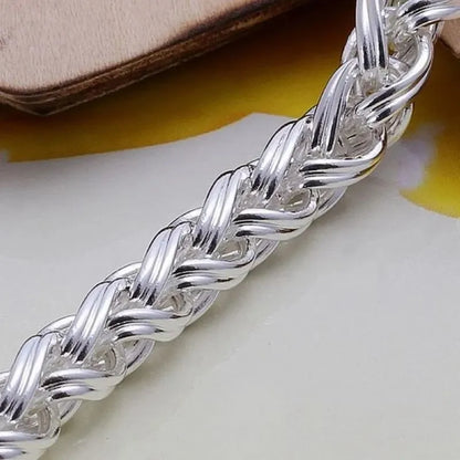 Extreme close-up of the silver wheat-chain bracelet's woven texture, propped against a leather-like surface.