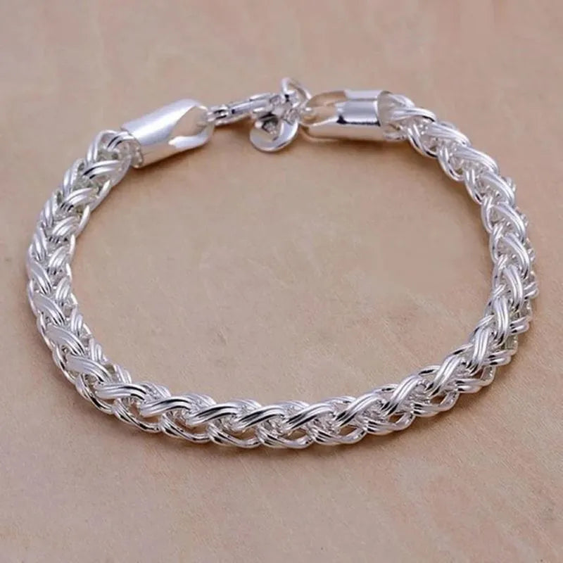 Silver wheat-chain bracelet laid in a circle on a tan surface, showing its thick woven texture and lobster clasp.