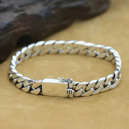 Close-up of the silver Cuban-link bracelet's polished links, laid on a tan suede surface with a dark rock prop.